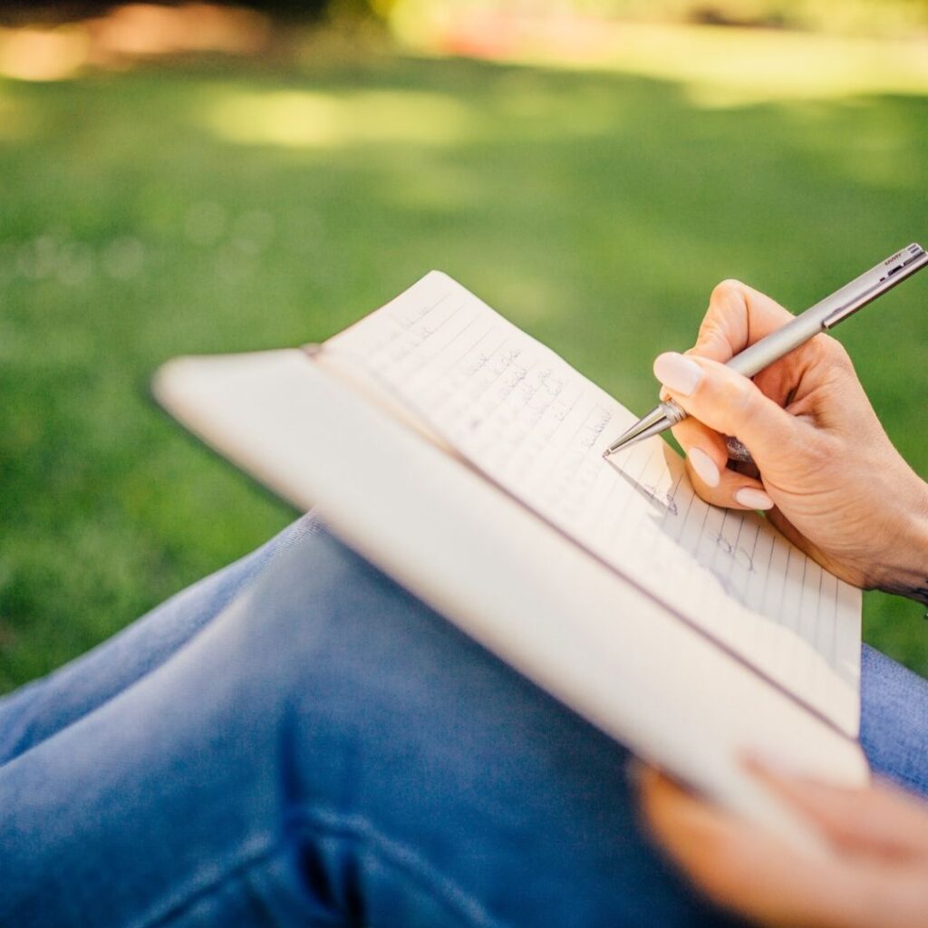 A woman sitting in the grass writing in a journal.