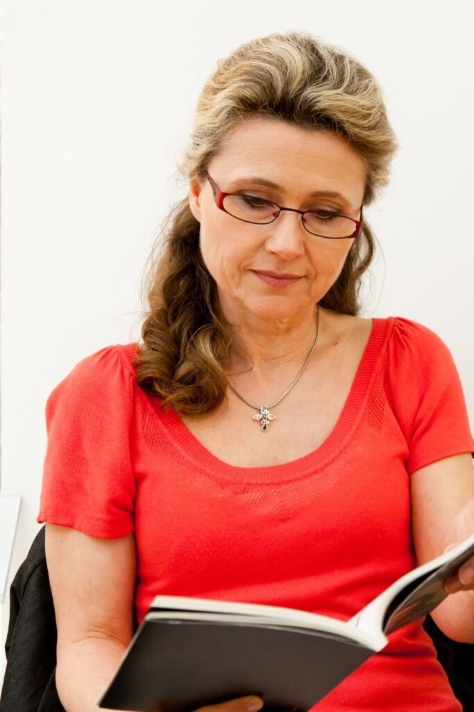 woman in red top and glasses reading a book.