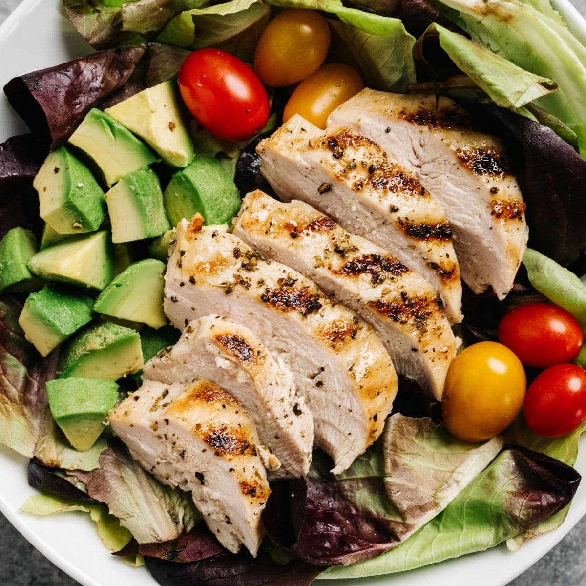 A bowl filled with sliced chicken, lettuce, cherry tomatoes and avocado chunks.