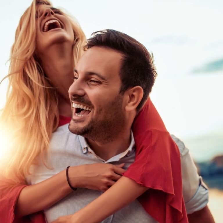 Blond woman on the back of a man with both of them laughing.