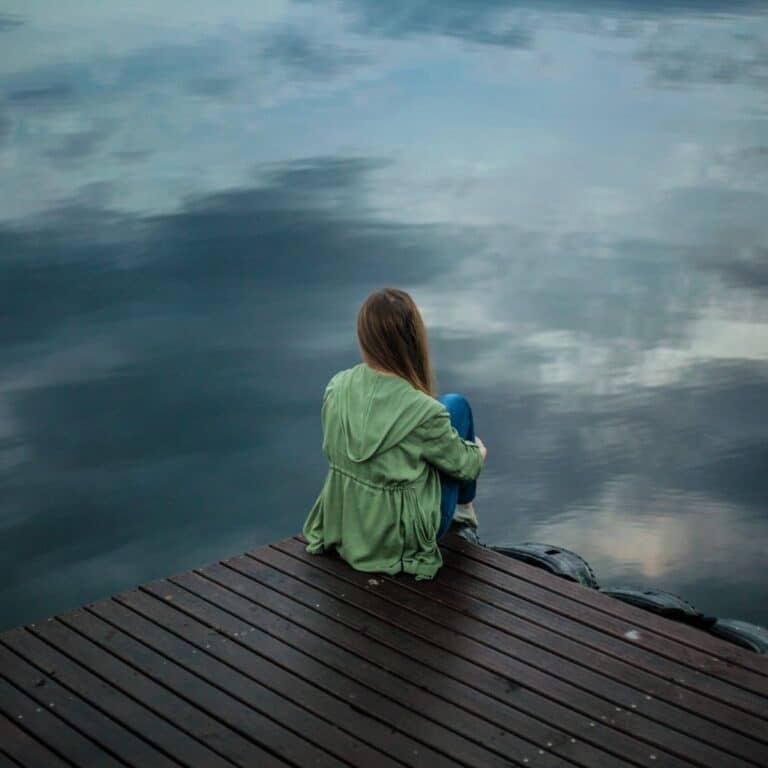 Woman sitting alone on a dock looking out at the water.