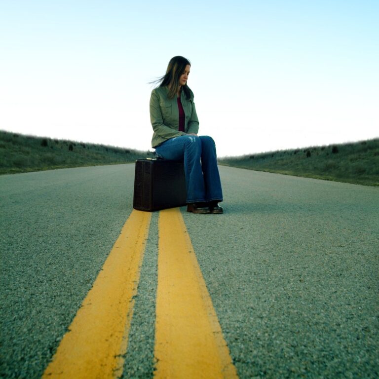 A dark haired woman sitting on a suitcase in the middle of the road - how to recover from rejection.